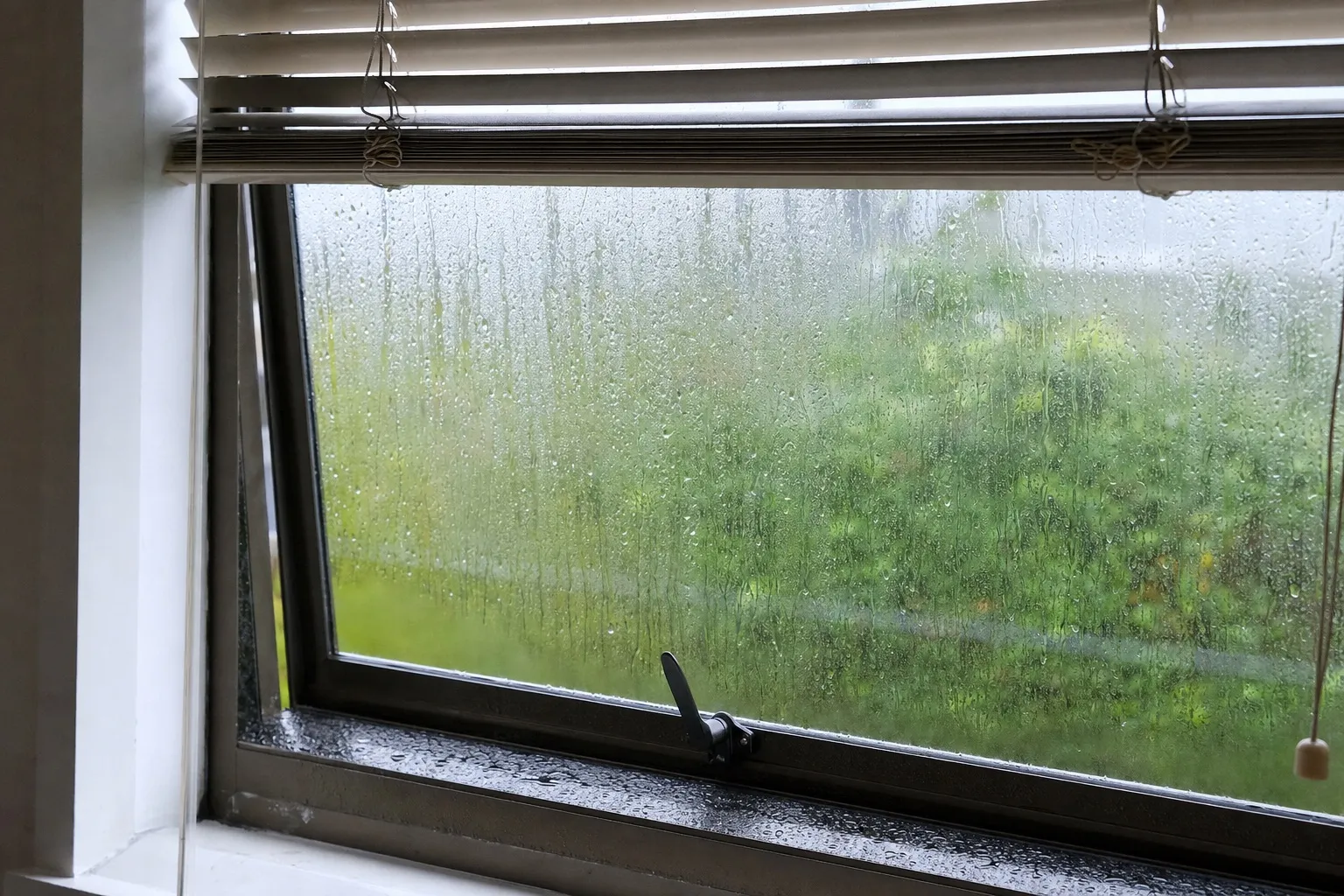 Illustrative: a 1980s bronze aluminium awning window with rain-wet glass and a venetian blind