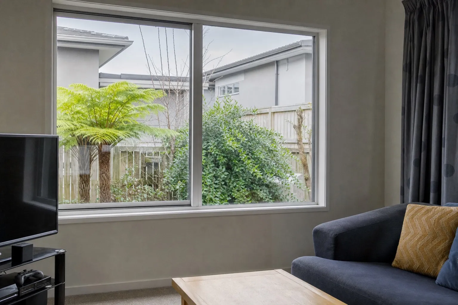 Illustrative: a slim aluminium double-glazed window in a 2000s townhouse living room, a neighbouring townhouse close behind